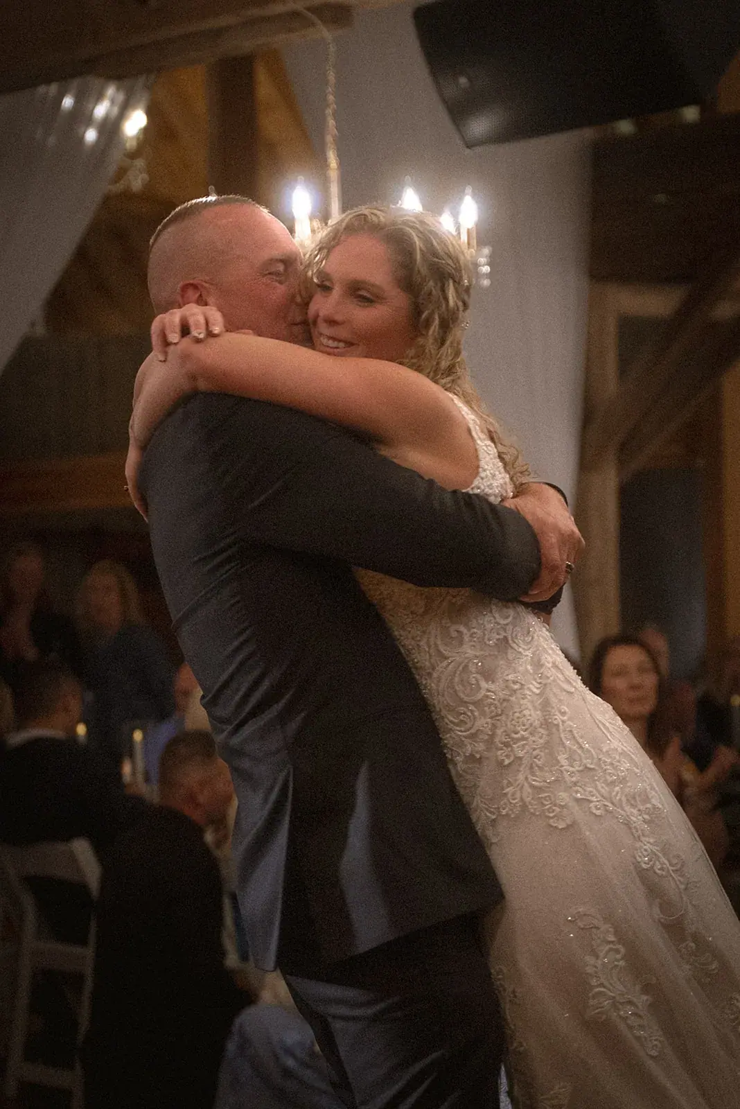 Bride and groom embracing during their first dance in a chandelier-lit barn