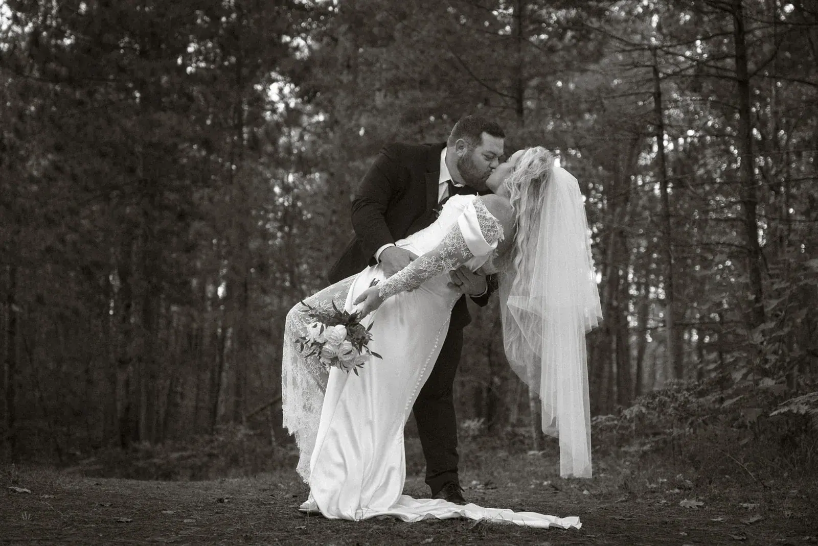Groom dipping bride pines in black and white — Ann & Brad's wedding at their log home in Vanderbilt