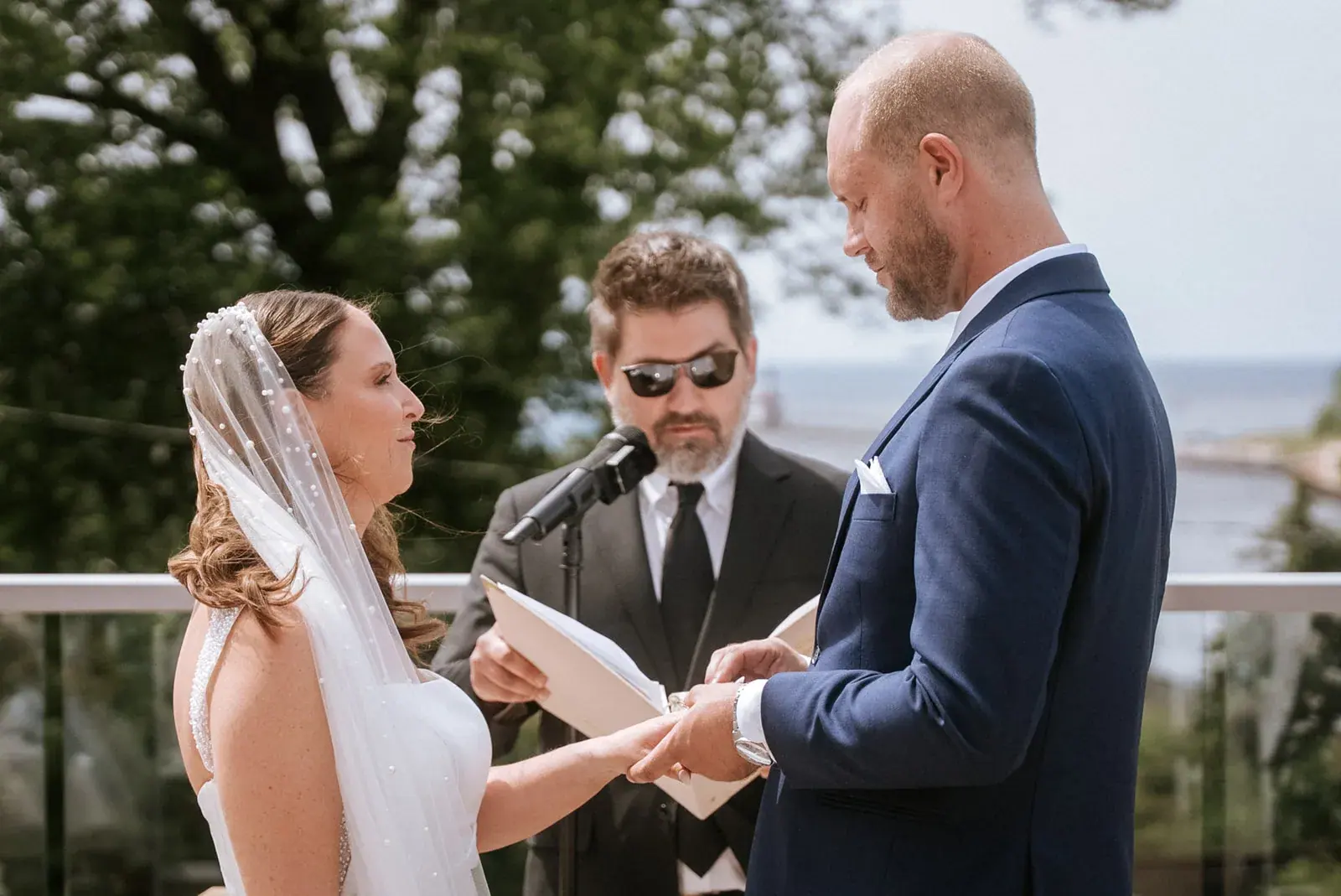 Bride and groom exchanging rings with a lake view behind them in St. Joseph, Michigan