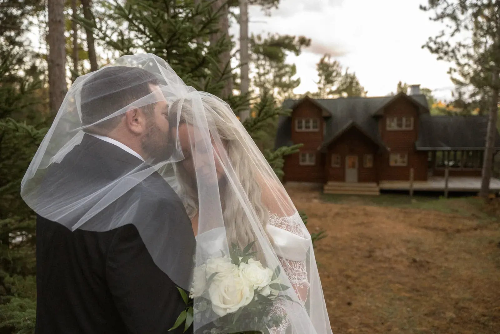 Vintage Nostalgia look: warm, filmic portrait of a couple kissing under the veil outside a log cabin